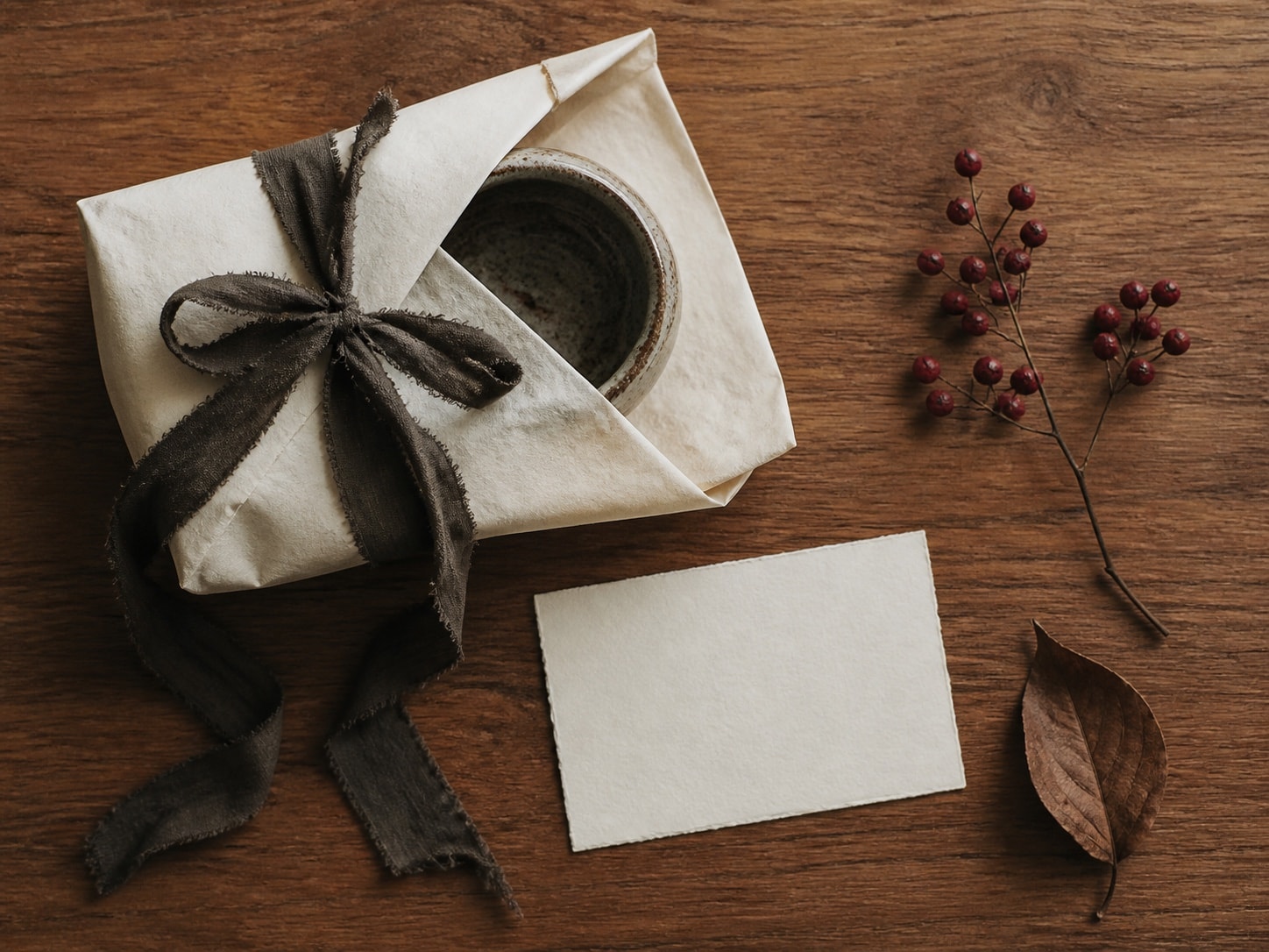 A small handmade object wrapped in plain paper and linen ribbon beside a blank note card